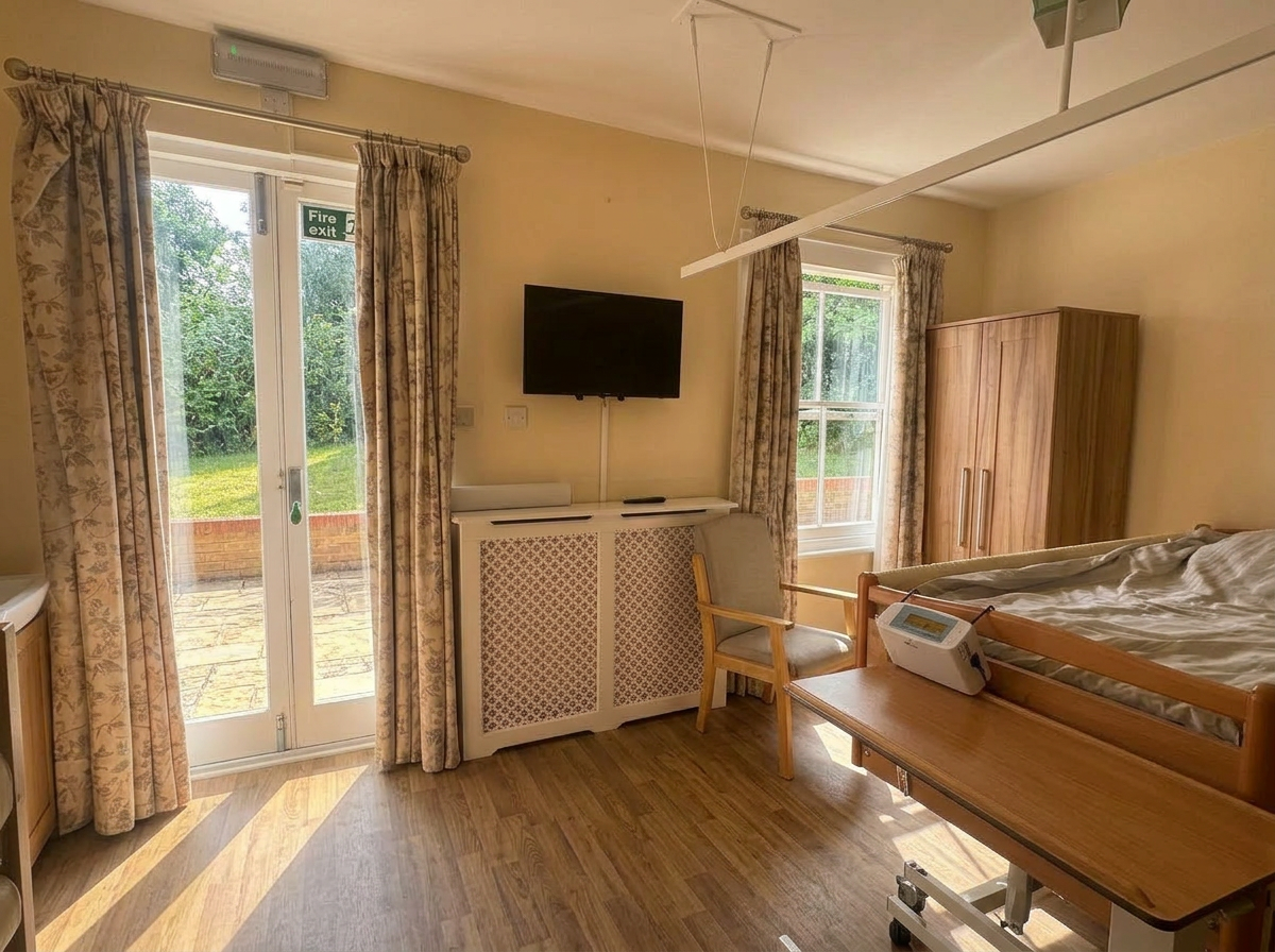Resident bedroom at St Anselm's with floor-to-ceiling french doors opening to the garden, a wardrobe and television, in warm natural light